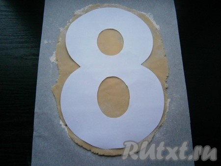 Одну часть теста раскатать сразу на пергаменте, подсыпав муку, или на силиконовом коврике. Вырезать шаблон из бумаги в виде восьмерки длиной около 20 см. Я вырезала из обычного листа А4. Раскатанное тесто должно быть толщиной около 0,5 см. Шаблон поместить сверху на тесто.
