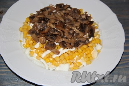 Грибы после жарки остудить. Затем на слой кукурузы выложить остывшие шампиньоны и слегка посолить.

