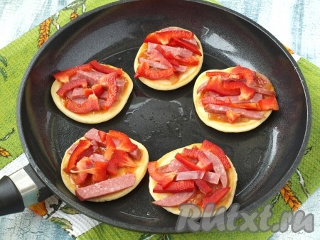 Готовить оладьи на среднем огне. Когда нижняя сторона поджарится, оладушки перевернуть, смазать верх кетчупом, выложить сверху часть нарезанных кусочков колбасы и болгарского перца.