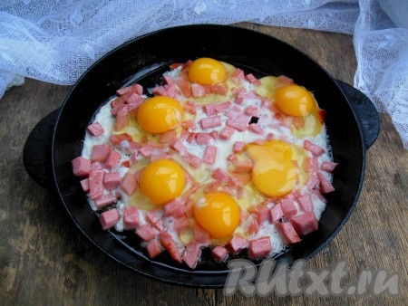 Вбейте в сковороду с обжаренной колбасой куриные яйца, стараясь сохранить целостность желтка.
