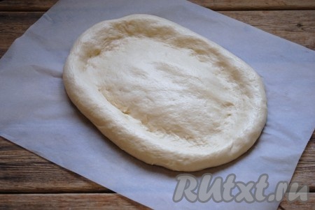 Противень застелить пергаментом и выложить тесто. Руками растянуть его в овальную лепёшку толщиной около 2 см. 