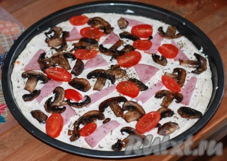 На тесто выложить обжаренные шампиньоны, нарезанную мясную нарезку и кружочки помидоров, посыпать приправой для пиццы.
