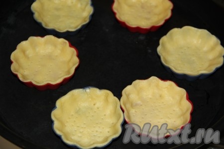 Готовое песочное тесто разделить на небольшие части и выложить в формочки с невысокими бортиками. У меня силиконовые формы, они очень удобны для выпекания корзинок, их поверхность не приходится перед выкладыванием теста смазывать маслом, так как силикон не пристает к готовой выпечке. Если у вас формочки металлические, то обязательно перед выкладыванием теста смажьте их растительным или размягченным сливочным маслом. Хорошо распределить тесто по поверхности формочек. Дно будущих корзинок наколоть зубочисткой.
