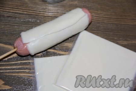 Обвернуть сосиску сыром и наколоть на палочку (как на фото).
