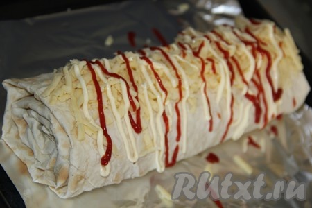 Готовый рулет переложить на противень, застеленный пергаментом или фольгой. По желанию, посыпать верх рулета сыром, натертым на крупной терке, и сделать решётку из майонеза и кетчупа.
