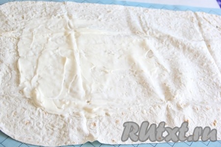 Вареное мясо пропустить через мясорубку. Лист лаваша смазать плавленым сыром, оставляя края чистыми.