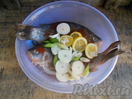 Карасей очистите от чешуи, удалите жабры и внутренности. Тщательно промойте рыбу под проточной водой. В глубокую миску поместите карасей, добавьте соль, смесь молотых перцев и паприку, выжатый из лимона сок, кружочки лимона, из которых выдавливали сок, очищенные и нарезанные кружочками головки чеснока, перемешайте, не забывая натереть рыбку и внутри.
