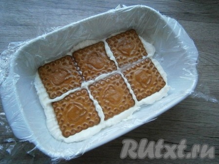 Квадратную или прямоугольную форму (у меня размер формы 18х12 см) застелить пищевой пленкой, чтобы края из формы свисали. Смазать дно формы несколькими столовыми ложками творожной массы и выложить печенье в один ряд.
