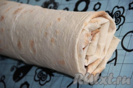 Аккуратно подвернуть боковые края лаваша на начинку, а затем, начиная с одной из неподвёрнутых сторон, свернуть лаваши с начинкой в плотный рулет. Завернуть рулет в пищевую плёнку и убрать в холодильник на 1 час.