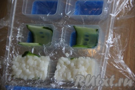 Рис залить водой 1 к 2 (на 100 грамм риса потребуется 200 мл воды). Варить рис на среднем огне под крышкой минут 15-20 с момента закипания (вода должна полностью испариться). Если хотите, то можете в сваренный рис добавить по вкусу рисовый уксус. Огурец вымыть и нарезать с помощью овощечистки на тонкие слайсы. Выстелить форму для льда пищевой плёнкой. Полоски огурца выложить в каждую лунку формы (как на фото).