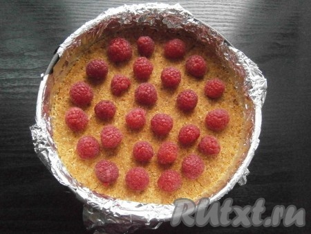 Достать из морозилки форму с крошкой, на застывший корж выложить половину малины.