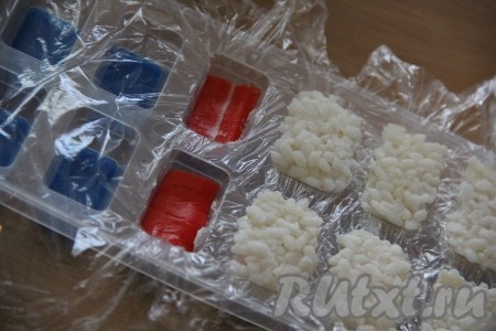 Крабовые палочки развернуть, нарезать на кусочки по размеру лунок для льда. Выложить кусочки крабовых палочек поверх сыра и плотно прижать.
