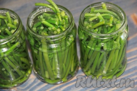 Банки предварительно вымыть и простерилизовать удобным для вас способом. На дно каждой банки выложить по 1 лавровому листу, по одной горошинке душистого перца и по 2 горошины чёрного перца. Плотно выложить в банки чесночные стрелки.
