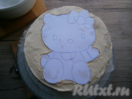 Теперь распечатайте на принтере на белой бумаге картинку Китти или нарисуйте на листе белой бумаги, чтобы она вмещалась на торте. Картинку вырезать и поместить на верх торта. Обвести контуры зубочисткой.
