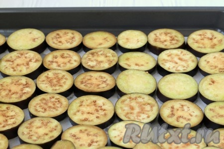 На противень, застеленный пергаментом, выложить в один слой плотно друг к другу кружочки баклажанов. В небольшую ёмкость налить растительное масло и, окуная в него кисточку, хорошо смазать маслом все кружочки баклажанов. Я запекала в два захода.