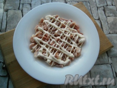 Копченый окорочок освободить от шкуры и костей, мясо нарезать кусочками и выложить на тарелку или в салатник первым слоем. Сверху нанести сеточку из майонеза.
