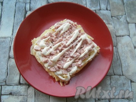 На картофель выложить слой нарезанной кубиками колбасы, нанести сеточку из майонеза.
