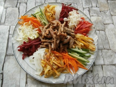 Огурцы и помидоры нарезать тонкой соломкой, свеклу очистить и натереть на корейской или обычной крупной терке, лук отжать. Далее на большую тарелку выкладывать овощи (лук, свеклу, капусту, помидоры, картофель, огурцы, морковь) горками по кругу, чередуя цвета, а в центр выложить жареное мясо.