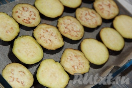 Противень (или форму для запекания) застелить пергаментом и смазать растительным маслом. Баклажаны вымыть и нарезать на кружочки толщиной, примерно, 6-7 мм. Выложить кружочки баклажанов на пергамент.
