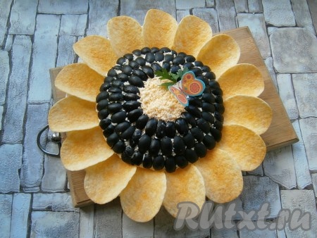 Далее украсить салат сверху четвертинками оливок, выложив их аккуратно в 3 ряда, серединку сверху оставить открытой. Салат "Подсолнух" поместить в холодильник на 1 час, после чего украсить по кругу чипсами.
