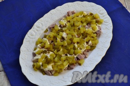 Вторым слоем выложить маринованные огурцы, нарезанные на небольшие кубики.