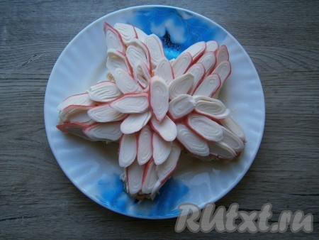 Крабовые палочки нарезать тонко наискосок, в результате получатся овальные кусочки. Верх салата украсить кусочками крабовых палочек.
