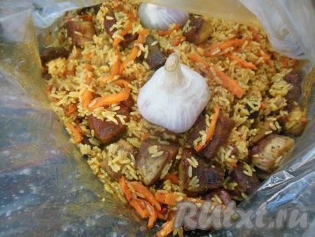 Переложите рис с мясом и овощами в рукав, добавьте целые головки чеснока (заранее промытые) вместе с шелухой. Чеснок придаст плову неимоверный аромат и вкус. Поместите рукав на противень.
