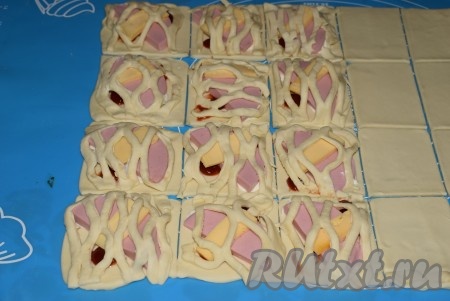 Каждый прямоугольник с колбасой и сыром накрыть сеточкой или полосками теста, нарезанными по размеру прямоугольников. Скрепить края теста каждой будущей слойки, прижимая пальцами по всему периметру прямоугольника.
