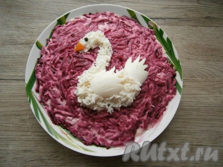 Далее следует украсить салат. Оставшиеся белки натереть на мелкой терке и выложить их сверху салата в форме лебедя, положить крыло и хвост из белка. Клюв вырезать из кусочка моркови, глазик сделать из горошины черного перца.
