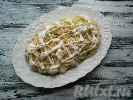 Далее выложить слой очищенного и натёртого на крупной тёрке картофеля, который немного посолить и поперчить, смазать майонезом.