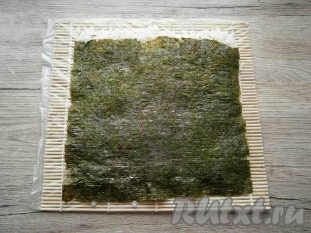 Теперь нужно аккуратно лист нори с рисом перевернуть. Это лучше сделать, конечно, с помощью еще одной циновки, накрыв ею рис и просто перевернув.&nbsp;
