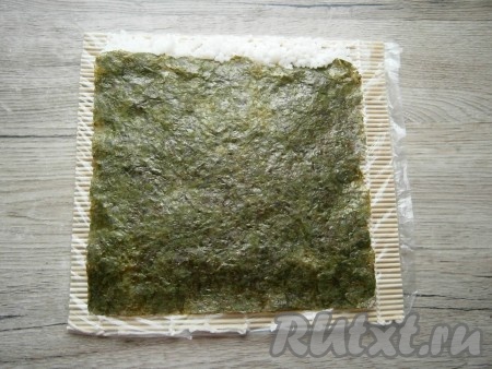 Аккуратно лист нори с рисом перевернуть (это лучше всего сделать используя вторую циновку). Затем выложить сверху листа полосочку риса шириной 1 см (как на фото).
