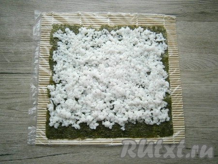 Рис распределить по всему листу нори тонким слоем, не доходя до нижнего края около 1 см (как на фото).
