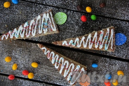 Я вставила в бисквитные пирожные палочки для мороженого, но можно обойтись и без них. Украсить наши новогодние ёлочки сахарной пудрой, цветной посыпкой или нанести рисунок сахарной глазурью (я украсила покупной сахарной глазурью в тюбике).
