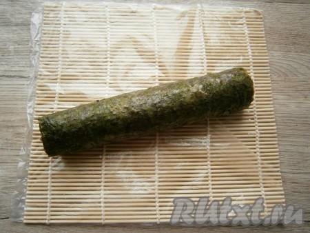Аккуратно и плотно, с помощью циновки, свернуть лист нори с начинкой в рулет.

