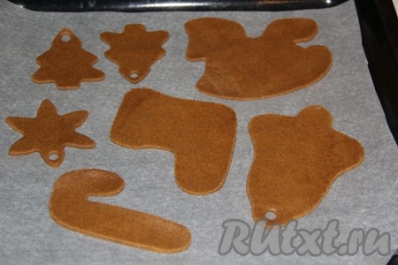 Готовое тесто достать их холодильника и тонко раскатать в пласт толщиной, примерно, 2-3 мм. Вырезать фигурки в виде ёлочек, колокольчиков или снежинок (печенье в виде разных фигурок можно вырезать с помощью формочек для печенья или трафаретов из картона). Переложить печенье на противень, застеленный пергаментом. Для того чтобы рождественское печенье можно было повесить на ёлку, нужно сделать отверстия для ленты (я сделала дурочку в каждом печенье с помощью толстой коктейльной трубочки). Для того чтобы не деформировать фигурки, отверстия лучше делать, когда печенье уже выложено на застеленный противень.
