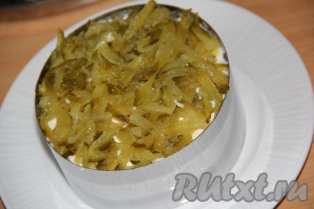 Маринованный огурчик натереть на крупной тёрке, затем отжать лишний сок. Натертый огурец выложить поверх белков.
