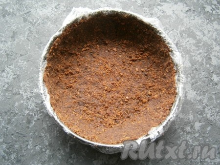 И дно, и бока формы диаметром 18 сантиметров застелить пищевой плёнкой, выложить печенье, хорошо его утрамбовать, формируя высокие бортики. Поместить форму в холодильник на час.