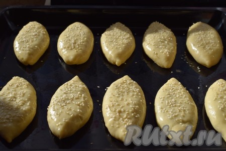 По желанию, посыпаем пирожки кунжутом, накрываем противень с пирогами пленкой и оставляем на расстойку на 20-30 минут.