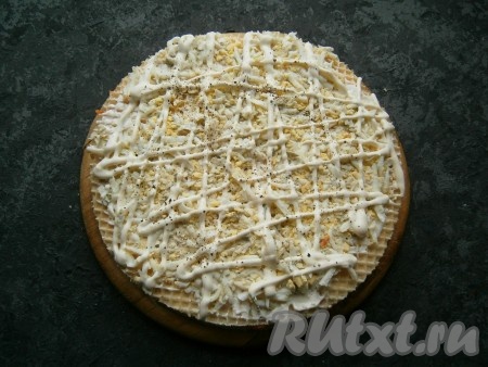 Далее выложить третий корж, смазать его сыром, разложить половину натертых яиц, поперчить, нанести сеточку из майонеза.
