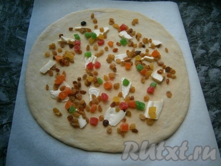 Тесто обмять с небольшим количеством муки, раскатать в пласт толщиной около 0,5-0,7 см, выложить изюм и цукаты. Если изюм очень сухой, то предварительно его замочите в кипятке на 10 минут и обсушите. Также по всему пласту теста разложить 20-30 грамм, нарезанного на небольшие кусочки, сливочного масла.