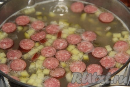 Соленые огурчики нарезать на кубики и добавить в кастрюлю. Варить рассольник с колбасой, перловкой и огурцами 5-7 минут.
