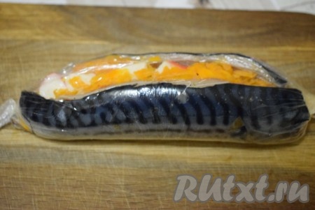 С помощью пищевой пленки (на которой лежала скумбрия) складываем филе скумбрии с двух сторон так, чтобы начинка оказалась внутри (то есть складываем филе, будто закрываем книгу). Скумбрию плотно оборачиваем пленкой так, чтобы начинка оказалась полностью внутри рыбы, перекручиваем концы пленки с двух сторон.
