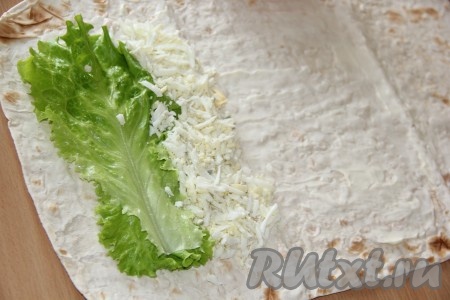 Листья салата вымыть и обсушить. Яйца предварительно сварить (в течение минут 10 с момента закипания воды), остудить, очистить и натереть на крупной тёрке. На край лаваша выложить два листа салата, рядом выложить полоску из натёртых яиц.
