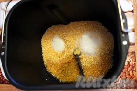 Первым делом вылить растительное масло на вращающуюся мешалку. Затем в контейнер хлебопечки высыпать кукурузную крупу, соль и сахар.