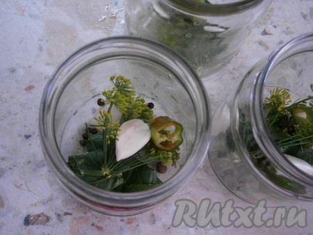 По простерилизованным баночкам разложить листья и корень хрена, укроп, очищенный чеснок, кусочки горького перца, горошины чёрного и душистого перцев.
