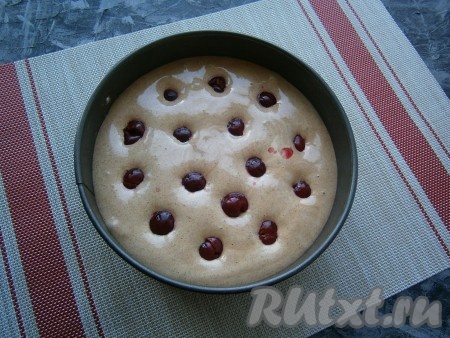 Застелить пергаментом дно разъёмной формы диаметром 18 сантиметров и выложить в неё бисквитное тесто, разровнять его. Свежую вишню вымыть, удалить косточки. Если вишня заморожена, тогда её нужно разморозить, удалить косточки, слить выделившийся сок. Распределить ягоды поверх теста. Выпекать шоколадный бисквит с вишней, примерно, 40-50 минут в разогретой до 180 градусов духовке. Готовность проверяйте сухой деревянной шпажкой (шпажка должна остаться сухой при прокалывании готового бисквита).