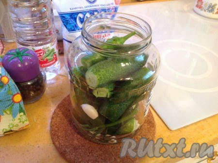 Аккуратно снимаем горячую банку, окутав полотенцем, и кладём в неё укроп, очищенный чеснок и кусочек острого перчика. Затем наполняем каждую банку огурцами с отрезанными кончиками.