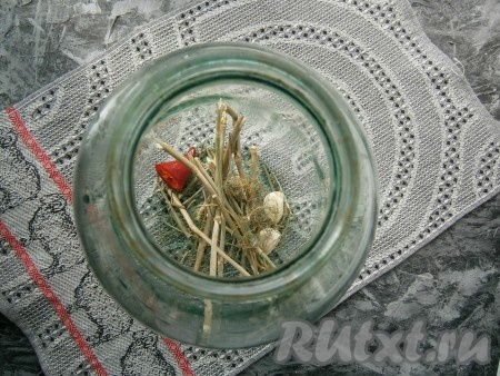 В чистую простерилизованную банку выложить очищенный чеснок, укроп и кусочек горького перца.
