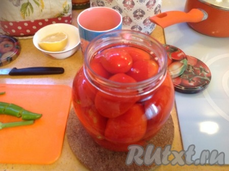 Раскладываем по предварительно простерилизованным банкам чеснок, стебли укропа и кусочек острого перчика. Укладываем помидоры плотно в банку. Заливаем кипятком.